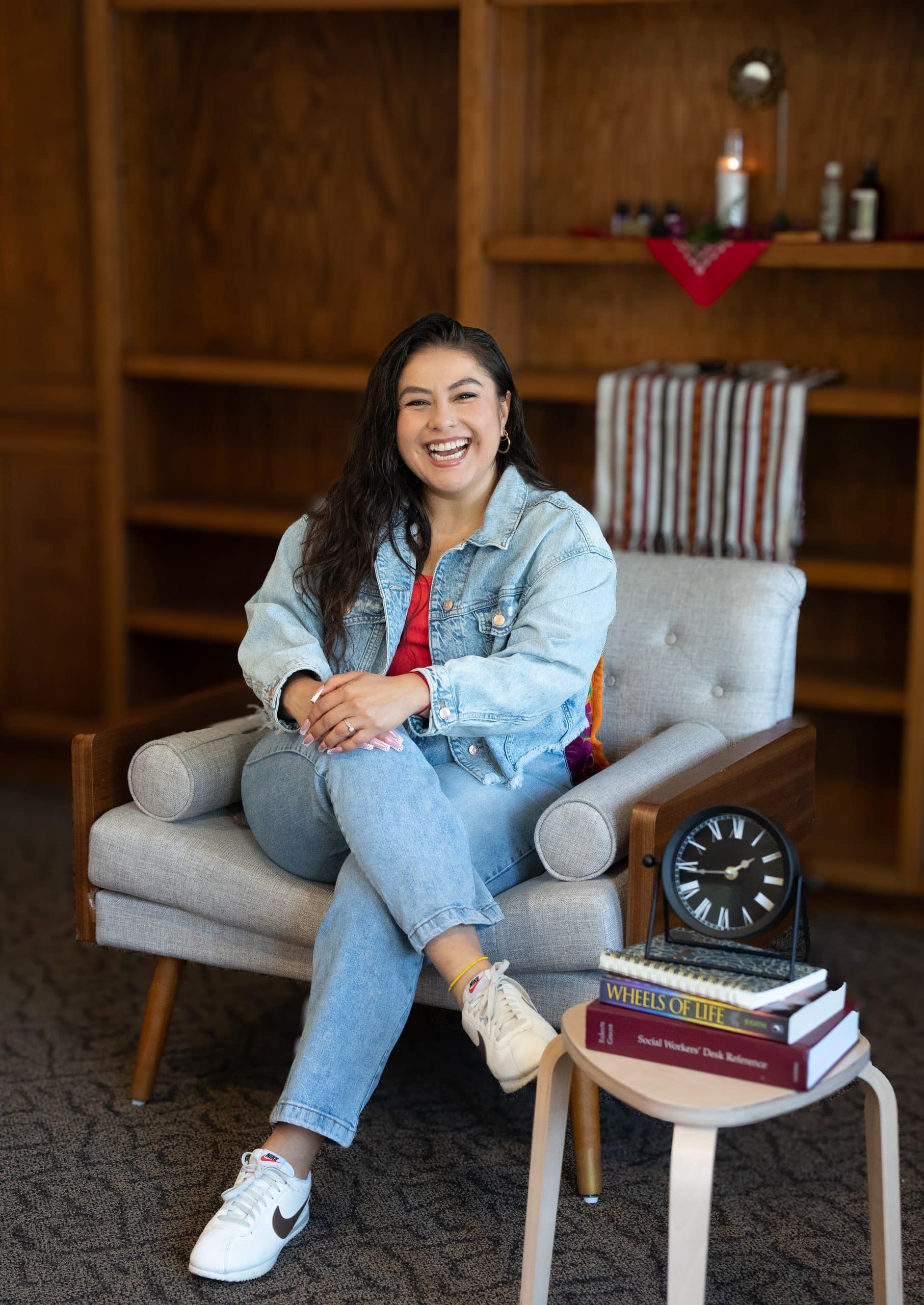 Andreina Zamudio LCSW, Long Beach therapist, smiling in her office surrounded by social work books and healing tools