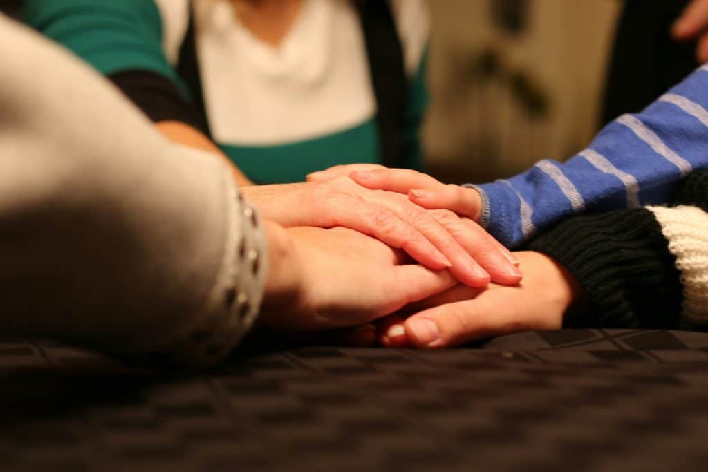 Close up of stacked hands from three people resting together at a table