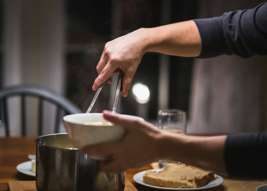 Hand using tongs to serve food from a pot at a home dinner table