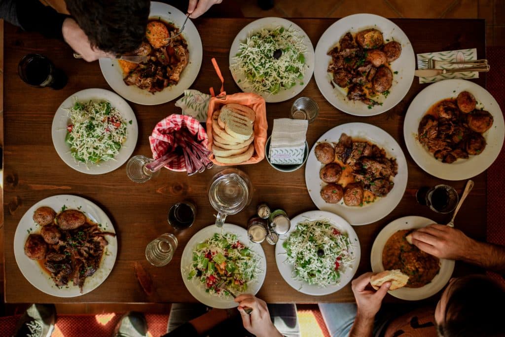 Overhead view of a shared family style dinner table with meat, salads, and bread