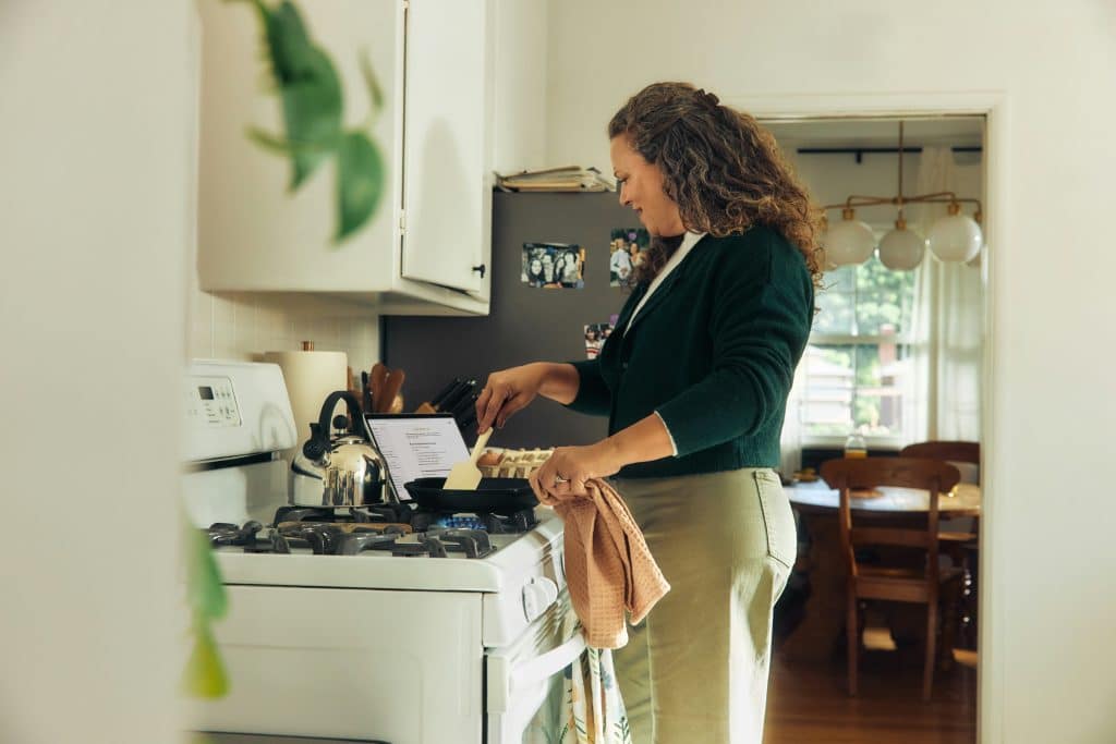Woman cooking on a stove while following a recipe on a tablet