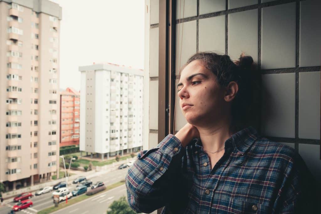 Woman looking out an apartment window with city buildings in the background