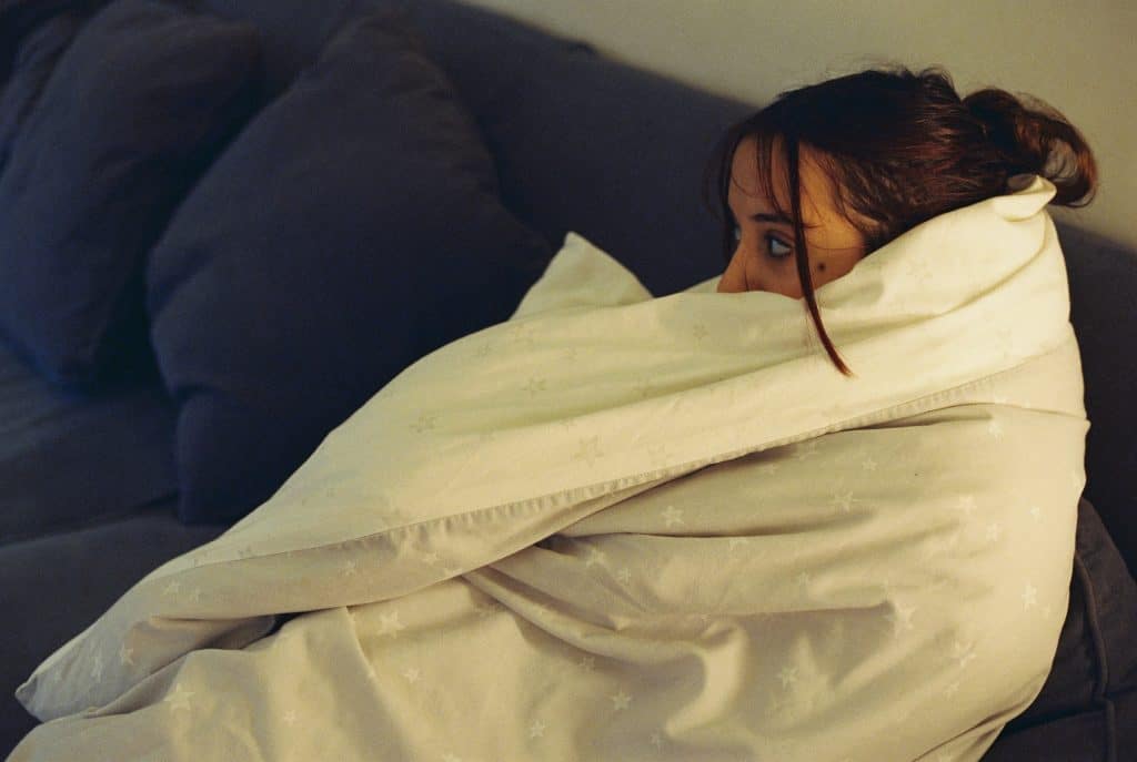 Woman lying awake on a couch wrapped in blankets, eyes open